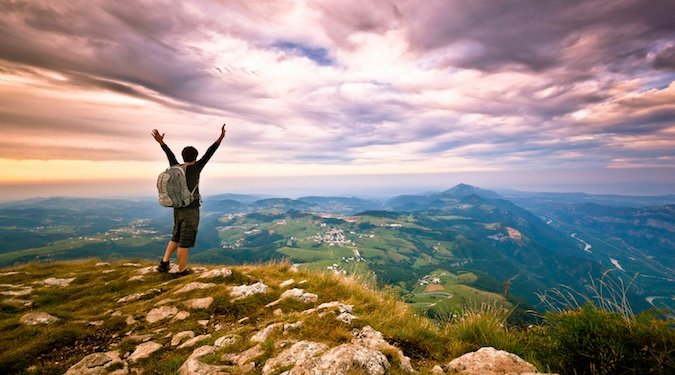 Nomadic backpacking hiker standing at the top of a mountain excited